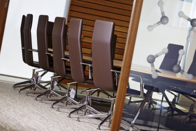 Обтянутые коричневой кожей стулья и фактурные деревянные поверхности в отделке стен одного из конференц-залов офиса и лаборатории фармацевтической компании в Кардиффе (административный округ Уэльс)