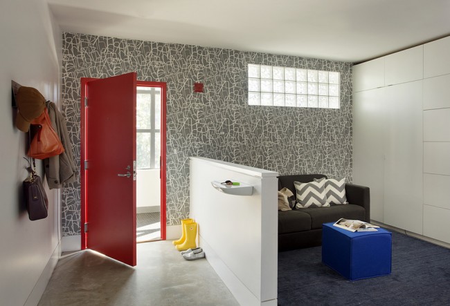 Серые обои на одной из стен в коридоре смотрятся достаточно современно в сочетании с ярко-красной дверью