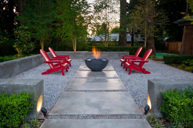Яркие красные стулья у декоративного костра в комфортной отделенной зоне отдыха небольшого сада