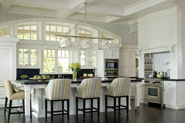 Кухня в классическом стиле с белым гарнитуром, черным матовым фартуком, бытовыми приборами из нержавеющей стали. Арочные окна подчеркивают общий стиль