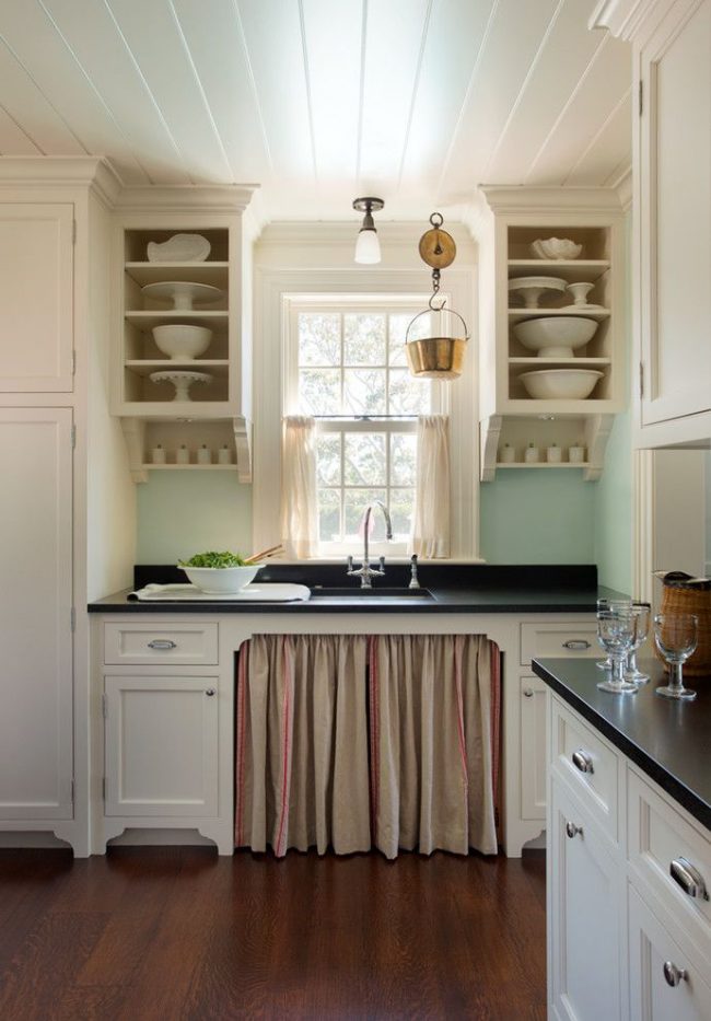 Кухня в пляжном стиле со свойственной цветовой палитрой: нежно-голубой кухонный фартук, белые фасады гарнитура, укороченные светло-песочные шторы на окнах и т.д.