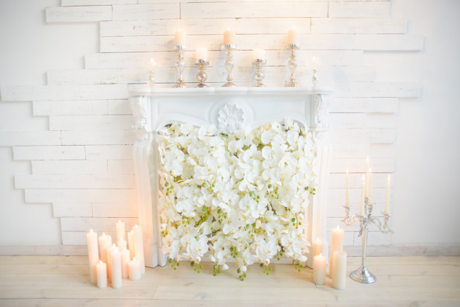 Белый резной каминный проем, украшенный цветами и свечами