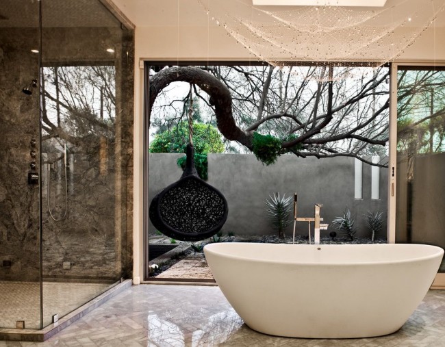 Черная круглая качель, подвешенная на дереве, идеально вписывается в интерьер сада и дополняет невероятный вид из панорамного окна ванной, хоть участок и глухо закрытый